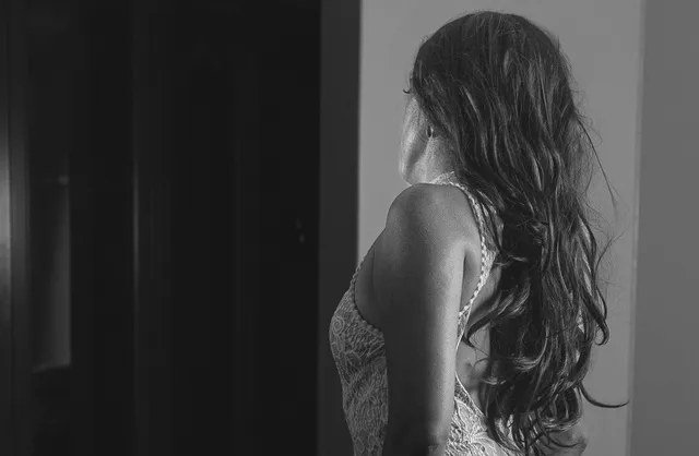 Long-haired girl in tight white dress kneeling in bedroom during intimate photoshoot